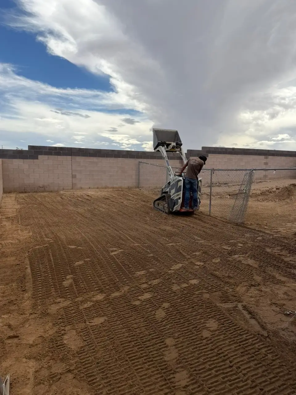 A J&J crew member finishing a graded backyard with the mini track loader