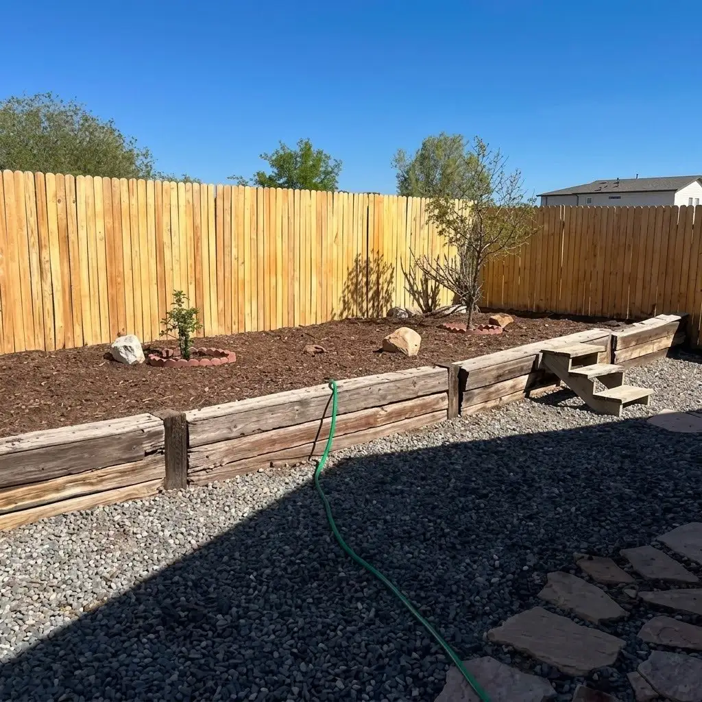New wood privacy fence above a timber raised bed with mulch, gravel, and flagstone
