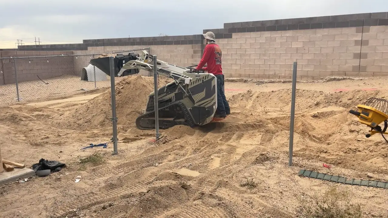 A J&J crew member grading a backyard with the mini track loader